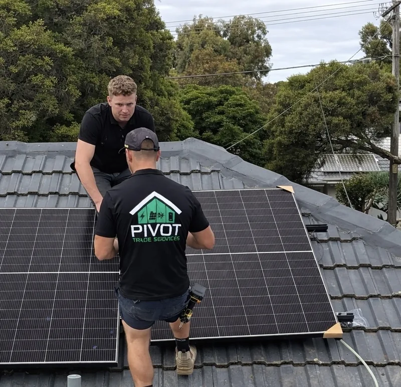 Two Pivot Trade Services electricians fitting solar panels on a tiled Melbourne roof