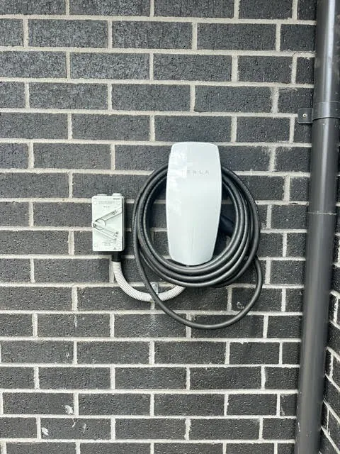 Wall-mounted home EV charger with a coiled tethered cable on a grey brick wall