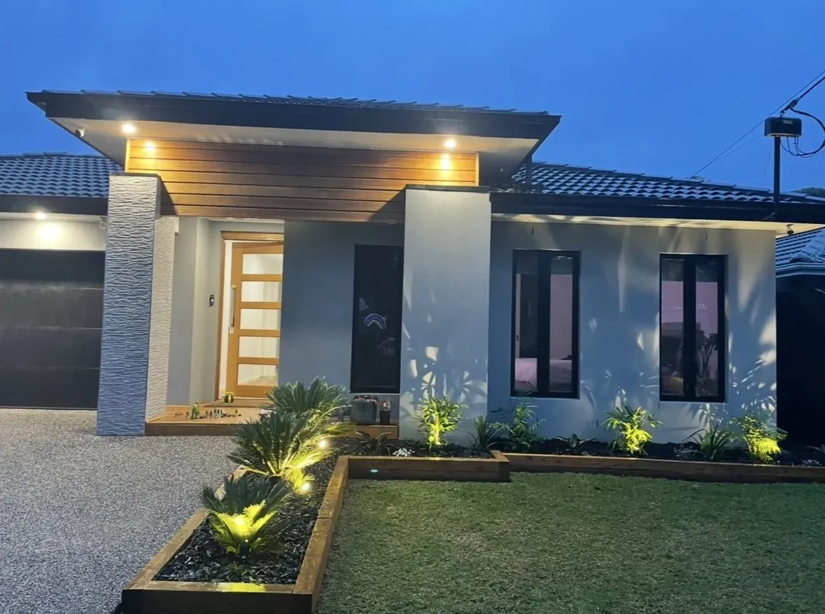 Modern single-storey home at dusk with garden uplighting and soffit lighting switched on
