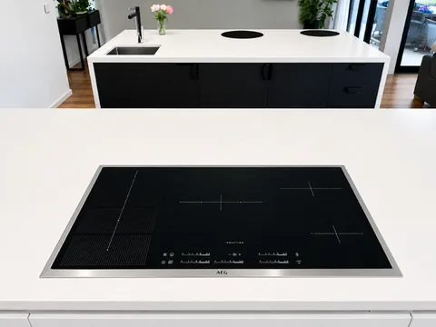 Black induction cooktop installed flush into a white stone kitchen benchtop