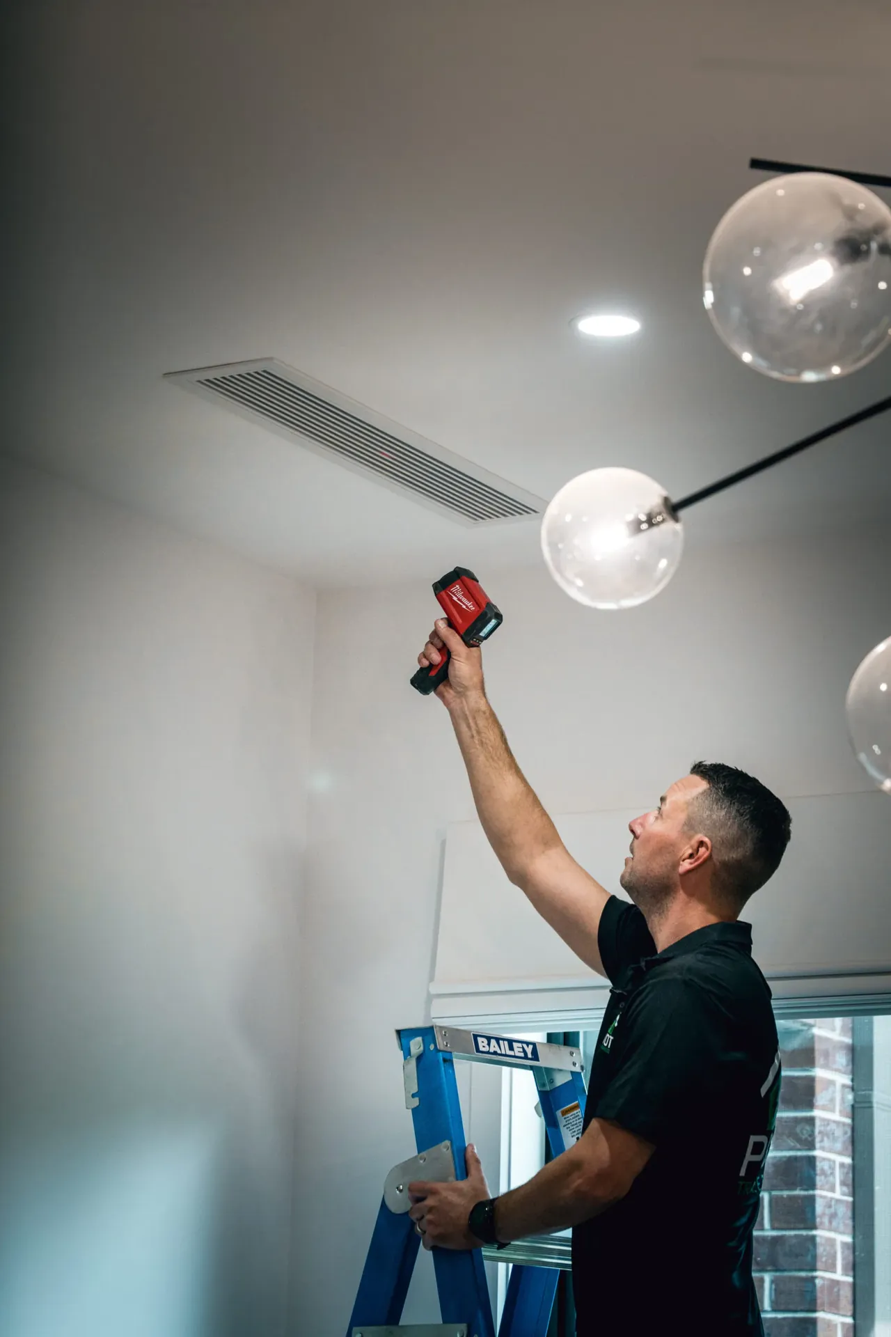 Pivot Trade Services electrician on a ladder installing pendant lighting in a renovated room