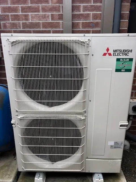 Mitsubishi Electric split system outdoor unit mounted on brick paving against a brick wall