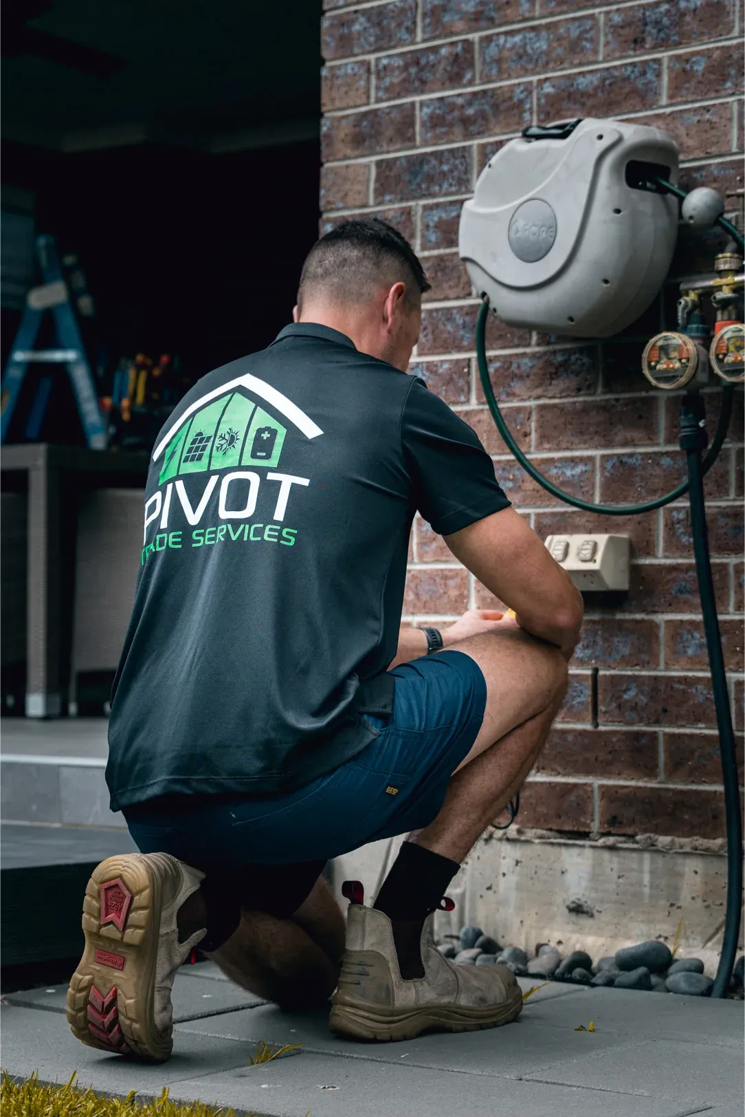 Pivot Trade Services electrician working at an outdoor air conditioning unit beside a brick wall