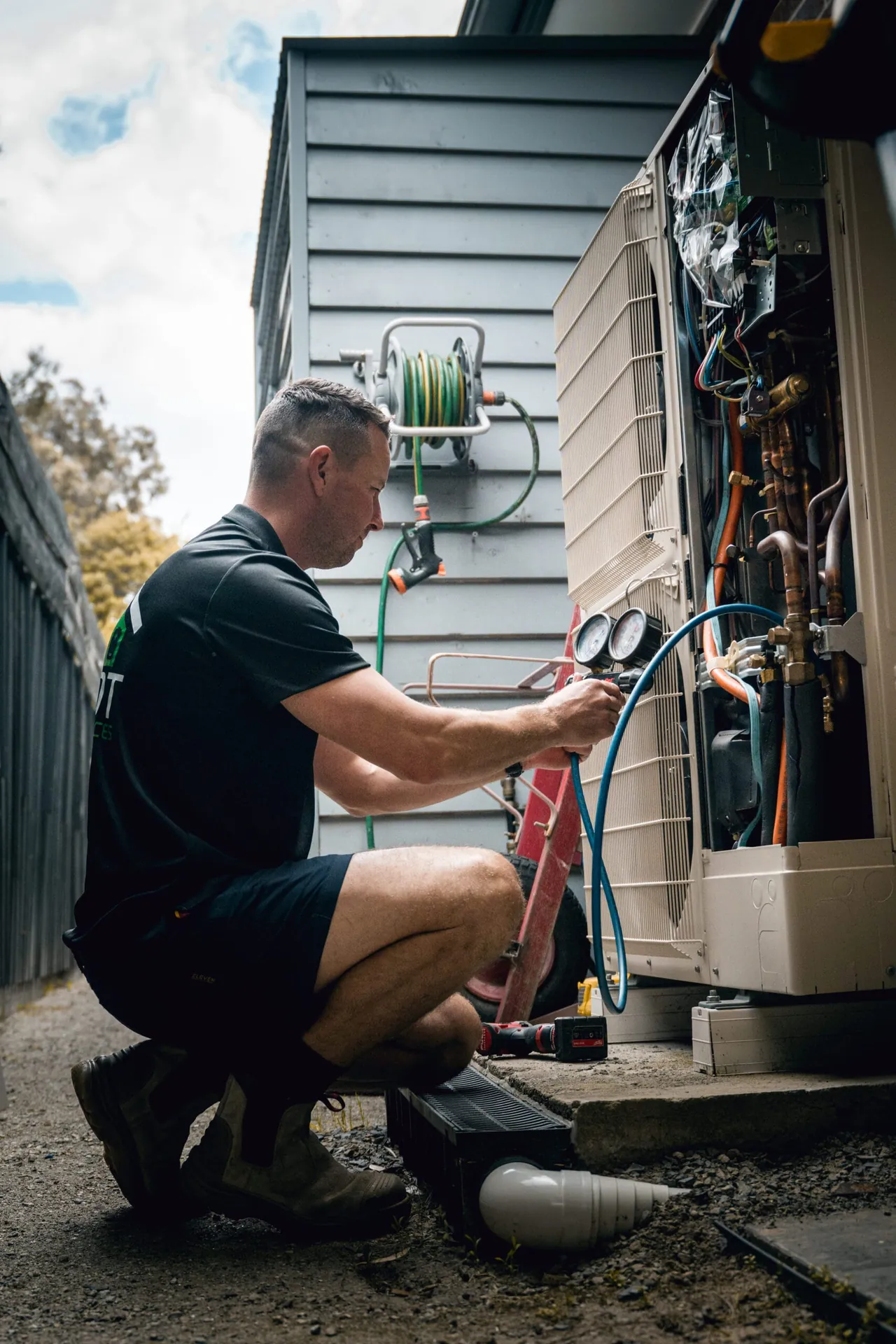 Pivot Trade Services technician servicing an outdoor air conditioning unit with refrigerant gauges