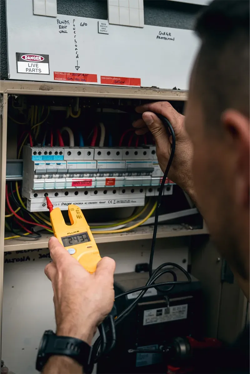 Pivot Trade Services electrician testing circuits inside a switchboard with a digital multimeter